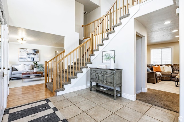 stairway with tile patterned floors, a high ceiling, and baseboards