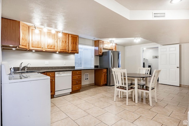 kitchen with washer / clothes dryer, freestanding refrigerator, a sink, dishwasher, and dark countertops