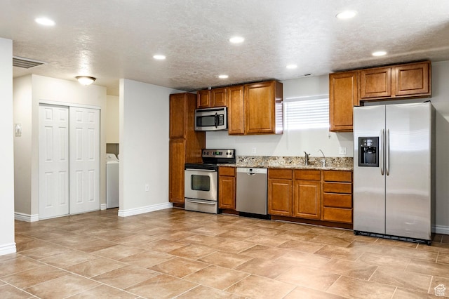 kitchen with brown cabinets, washer / clothes dryer, recessed lighting, stainless steel appliances, and light stone countertops