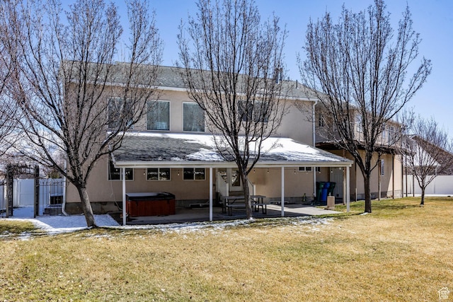 rear view of house with a patio area, a lawn, stucco siding, and a hot tub