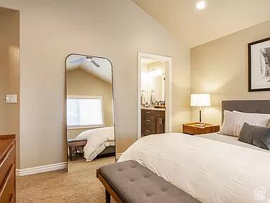 bedroom with light colored carpet, ensuite bathroom, baseboards, and vaulted ceiling
