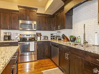 kitchen with light stone countertops, light wood finished floors, stainless steel appliances, decorative backsplash, and dark brown cabinetry