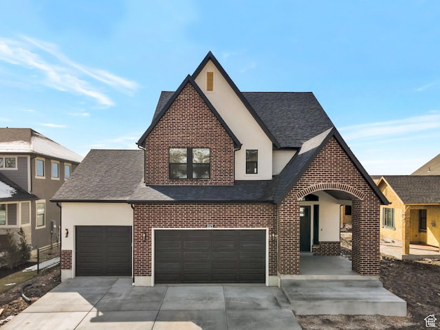 view of front of home featuring a shingled roof, concrete driveway, stucco siding, and brick siding