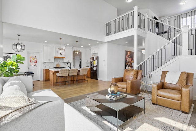 living area featuring baseboards, light wood-style flooring, a high ceiling, recessed lighting, and stairs