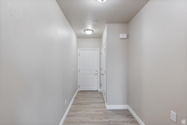 hall with a textured ceiling, light wood-style flooring, and baseboards