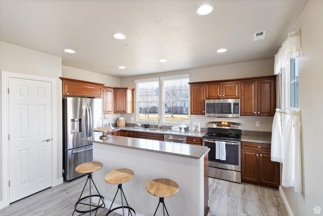 kitchen with stainless steel appliances, a kitchen island, light wood finished floors, a breakfast bar, and recessed lighting