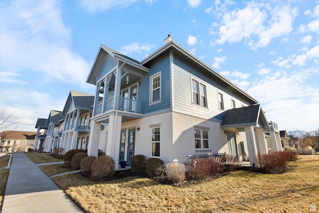 view of side of property featuring a balcony, stucco siding, and a chimney