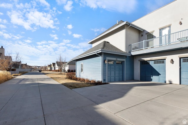 view of property exterior with a balcony, concrete driveway, an attached garage, stucco siding, and a residential view