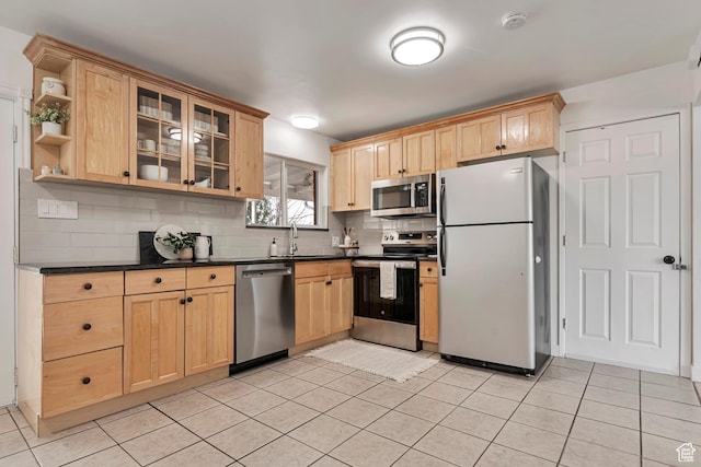 kitchen with dark countertops, tasteful backsplash, light brown cabinetry, a sink, and stainless steel appliances