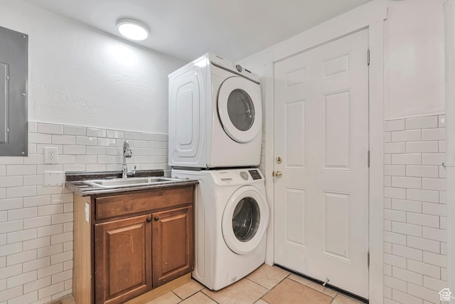 laundry room featuring cabinet space, stacked washer and dryer, light tile patterned flooring, a sink, and tile walls