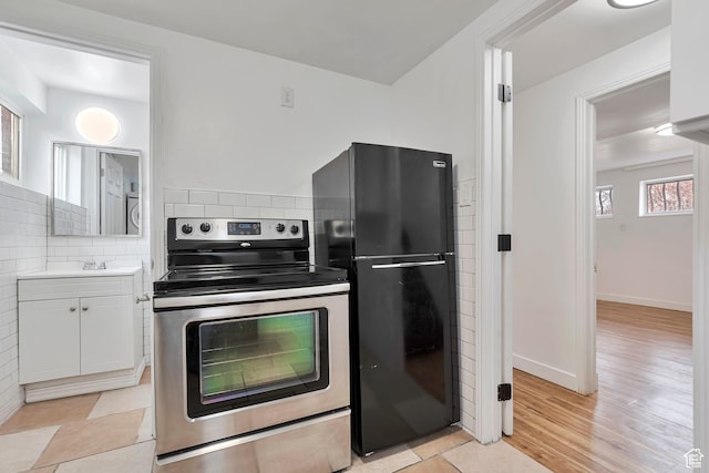 kitchen featuring decorative backsplash, white cabinets, freestanding refrigerator, light wood finished floors, and electric stove
