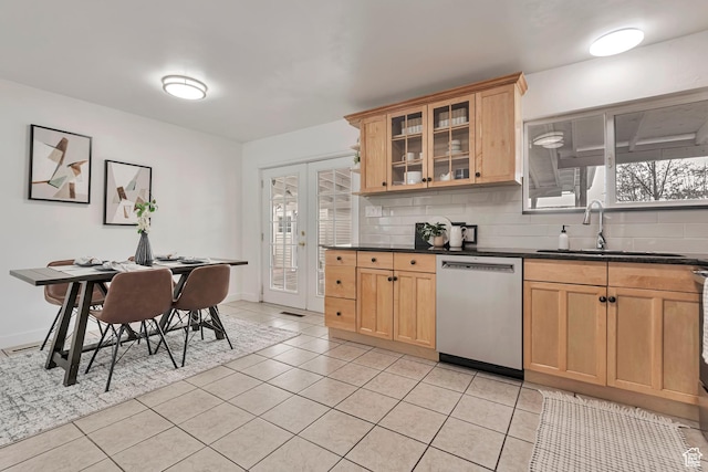 kitchen with stainless steel dishwasher, dark countertops, decorative backsplash, and a sink