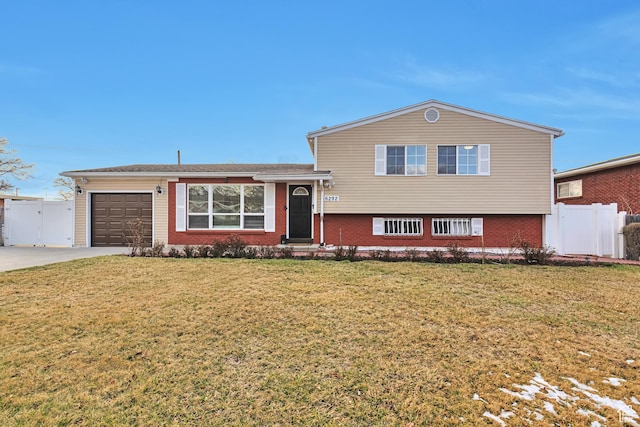 tri-level home featuring a front yard, concrete driveway, an attached garage, and fence