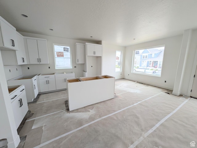 7077 W Granbury Dr S Unit 257, South Jordan, UT 84009 - kitchen with healthy amount of natural light, a center island, white cabinetry, a textured ceiling, and concrete floors