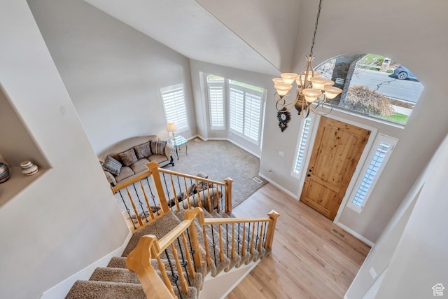 foyer entrance with a chandelier, a towering ceiling, visible vents, and light wood-style flooring