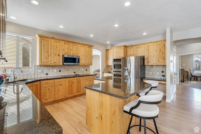 kitchen featuring a center island, arched walkways, a sink, a breakfast bar, and stainless steel appliances