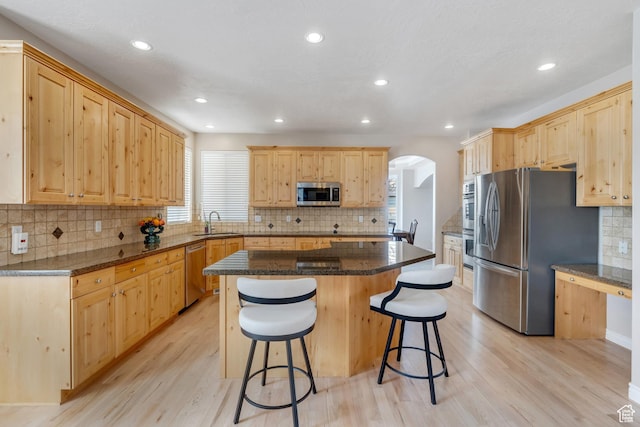 kitchen featuring arched walkways, light brown cabinetry, a sink, stainless steel appliances, and a breakfast bar area