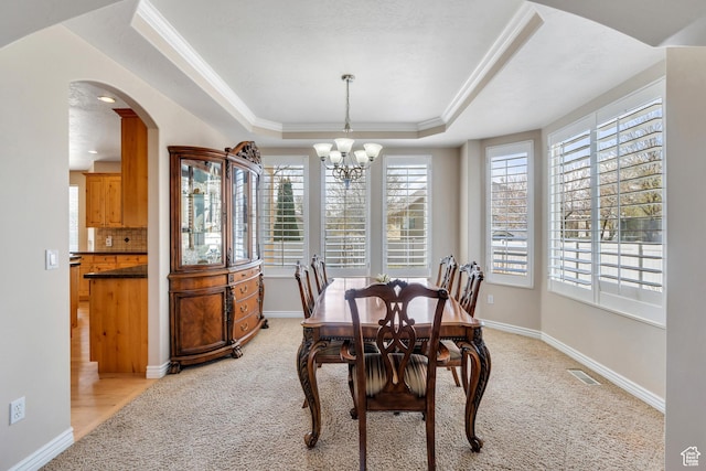dining space featuring a notable chandelier, light carpet, visible vents, a raised ceiling, and arched walkways