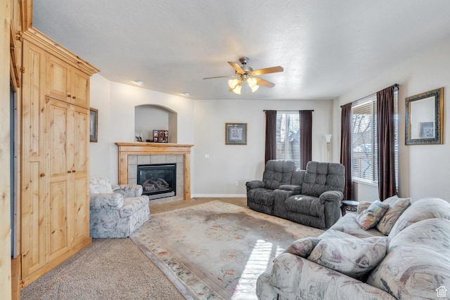 living area featuring baseboards, a tile fireplace, light colored carpet, and a ceiling fan