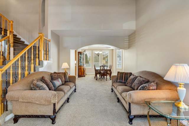 carpeted living room with a chandelier, arched walkways, a towering ceiling, and stairs