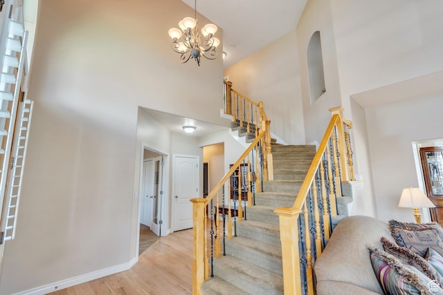 stairs featuring baseboards, an inviting chandelier, a high ceiling, and wood finished floors
