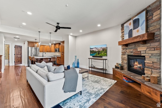 living area featuring a stone fireplace, recessed lighting, dark wood-style flooring, and ceiling fan