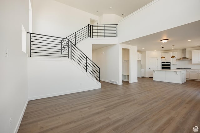 unfurnished living room with stairway, baseboards, wood finished floors, a towering ceiling, and recessed lighting