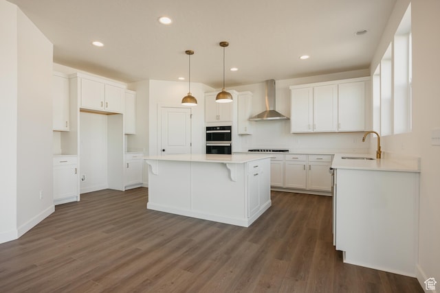 kitchen with wall chimney range hood, a sink, a center island, dark wood finished floors, and stovetop