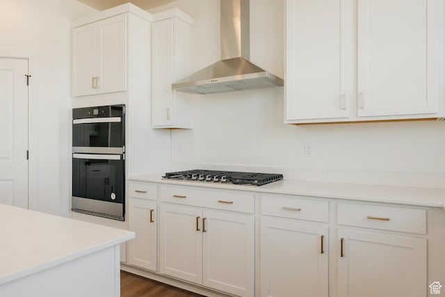 kitchen with wall chimney exhaust hood, stainless steel gas stovetop, double oven, and white cabinetry