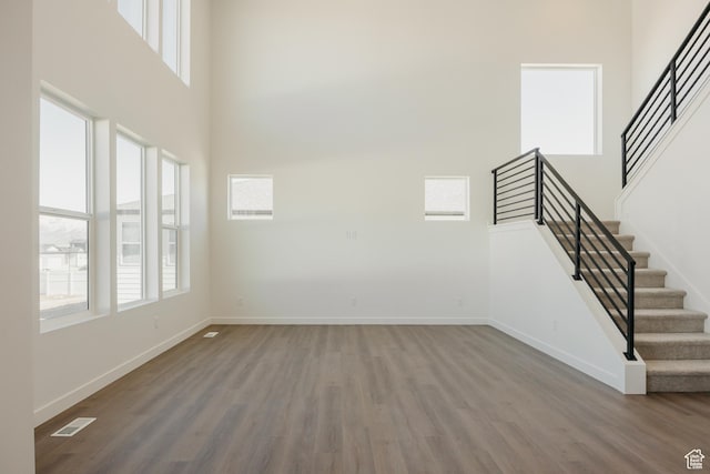 unfurnished living room featuring stairway, wood finished floors, baseboards, and a high ceiling