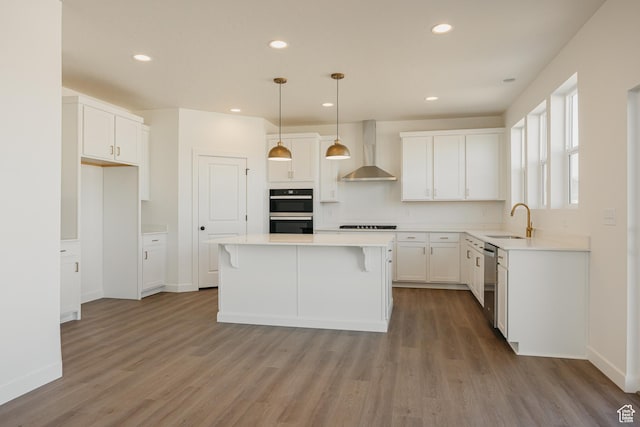 kitchen featuring wall chimney range hood, a sink, dishwasher, double wall oven, and wood finished floors