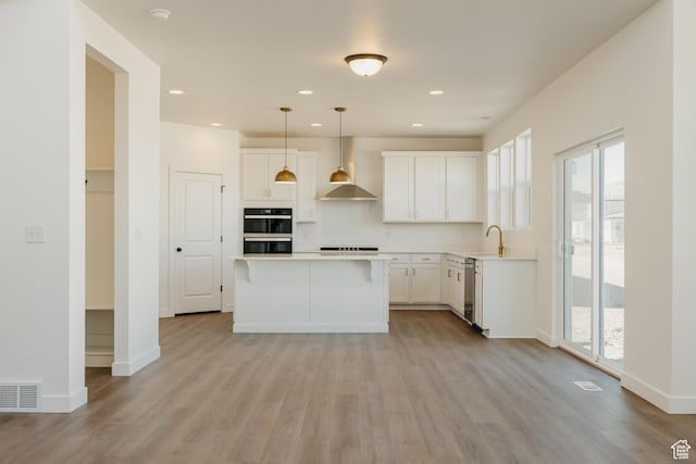 kitchen with wall chimney range hood, healthy amount of natural light, a sink, light countertops, and recessed lighting