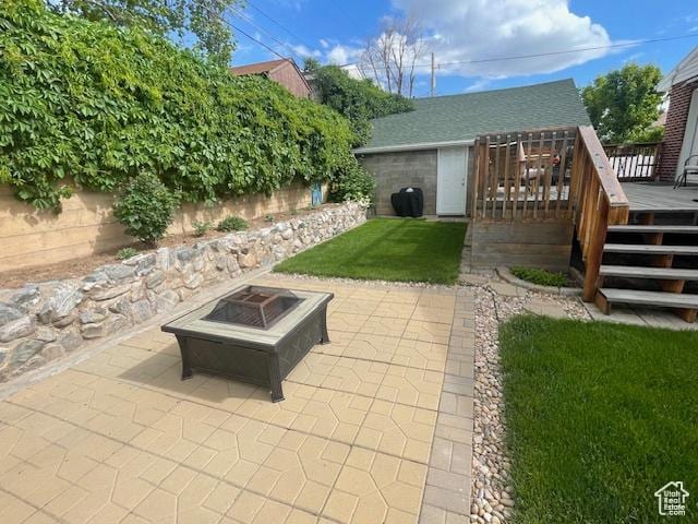 view of green lawn featuring a fire pit, a deck, and a patio