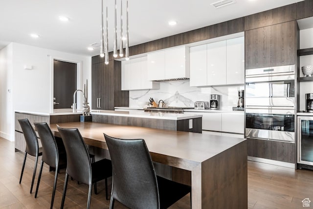 2752 W High Mountain Rd Unit 306, Park City, UT 84098 - kitchen featuring stainless steel double oven, a kitchen island with sink, decorative backsplash, white cabinets, and modern cabinets