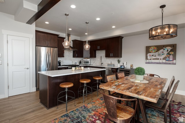8077 Courtyard Loop Unit 11, Park City, UT 84098 - kitchen featuring wall chimney exhaust hood, stainless steel appliances, dark brown cabinetry, a center island, and light wood-style floors