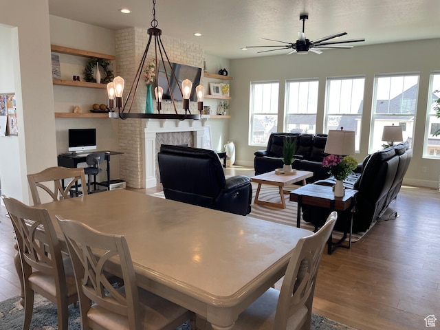 10887 S Lamond Dr, South Jordan, UT 84009 - dining space with baseboards, a large fireplace, wood finished floors, and ceiling fan with notable chandelier