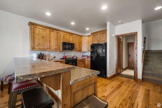 1056 W Lime Canyon Rd, Midway, UT 84049 - kitchen featuring light wood-style floors, a kitchen bar, a peninsula, black appliances, and decorative backsplash