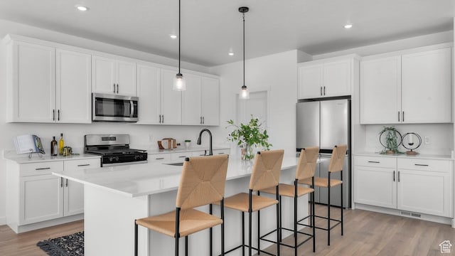 kitchen with stainless steel appliances, a center island with sink, light countertops, white cabinets, and light wood-style floors