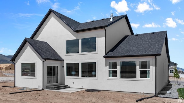 rear view of house featuring a shingled roof, stucco siding, and a mountain view