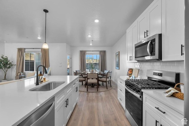 kitchen featuring a sink, tasteful backsplash, stainless steel appliances, light wood-style floors, and light countertops