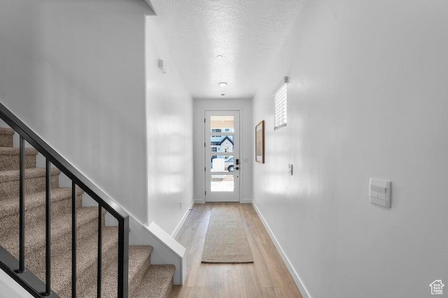 doorway to outside with light wood finished floors, stairway, a textured ceiling, and baseboards