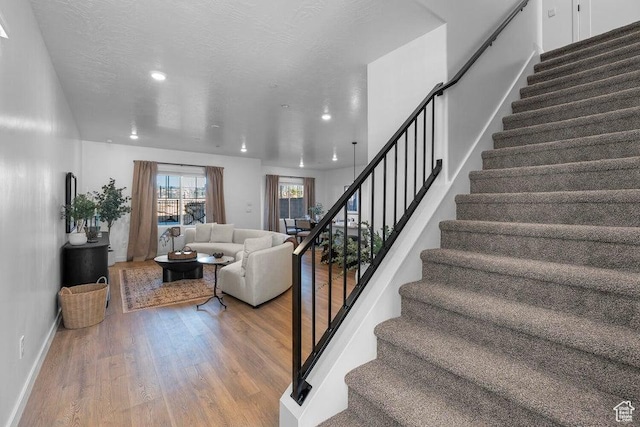 stairway featuring recessed lighting, baseboards, a textured ceiling, and wood finished floors