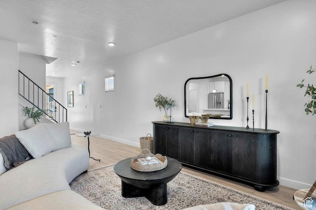 living room with stairs, light wood-style floors, baseboards, and a textured ceiling