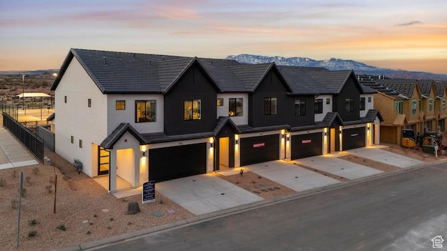 modern inspired farmhouse featuring an attached garage, fence, concrete driveway, stucco siding, and a mountain view