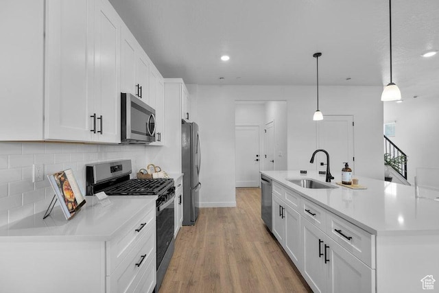 kitchen with a sink, decorative backsplash, stainless steel appliances, white cabinets, and light wood-style floors