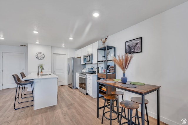 388 N Regatta Ln, Saratoga Springs, UT 84045 - kitchen featuring light wood-style flooring, a kitchen breakfast bar, stainless steel appliances, white cabinetry, and a sink
