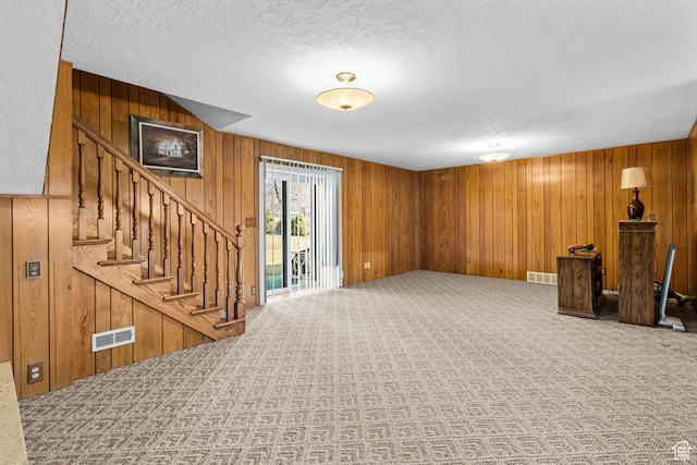 basement featuring stairs, visible vents, wooden walls, and carpet flooring