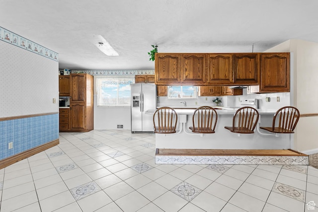 kitchen featuring wallpapered walls, a wainscoted wall, light countertops, stove, and stainless steel fridge