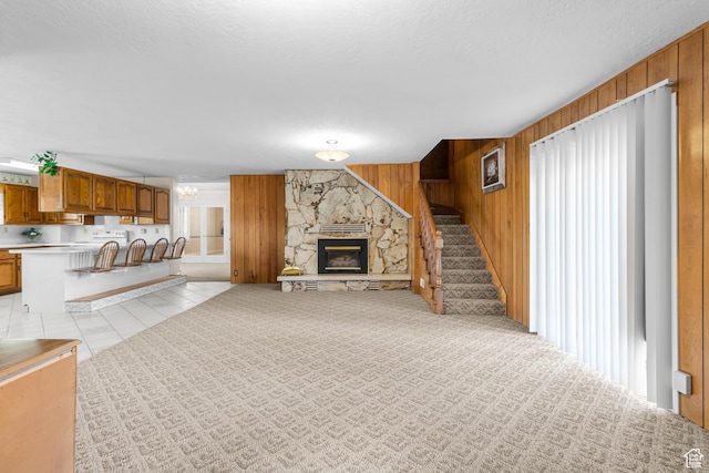 unfurnished living room featuring a wealth of natural light, wooden walls, stairway, and a stone fireplace