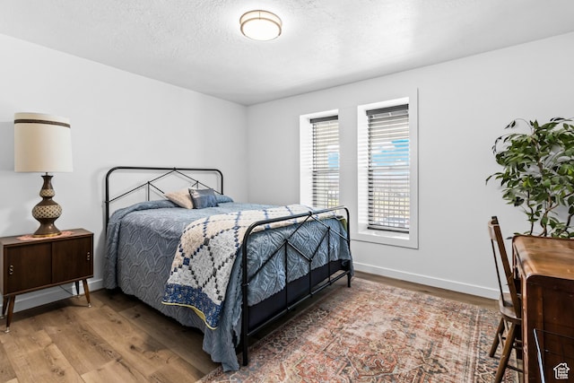 bedroom featuring a textured ceiling, baseboards, and wood finished floors